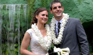 Happy newlyweds wearing leis in front of the waterfall following their wedding ceremony at the Mai-Kai.