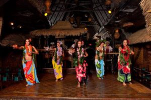 Five female Polynesian Dancers caught in mid-dance wearing colorful traditional attire.