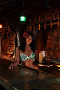 Sarong clad Mai-Kai maiden displays a tray of classic Mai-Kai cocktails from behind the candlelight Molokai bar.